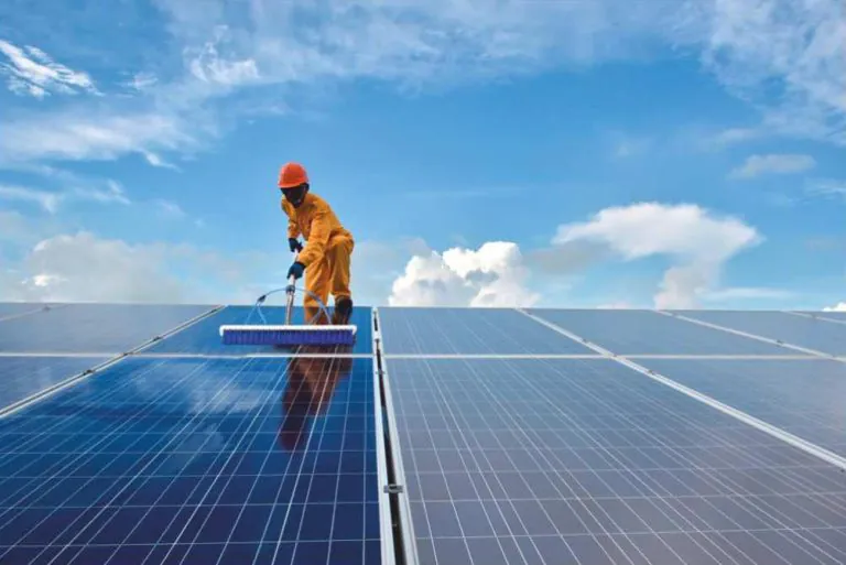 Worker using a soft brush to clean solar panels